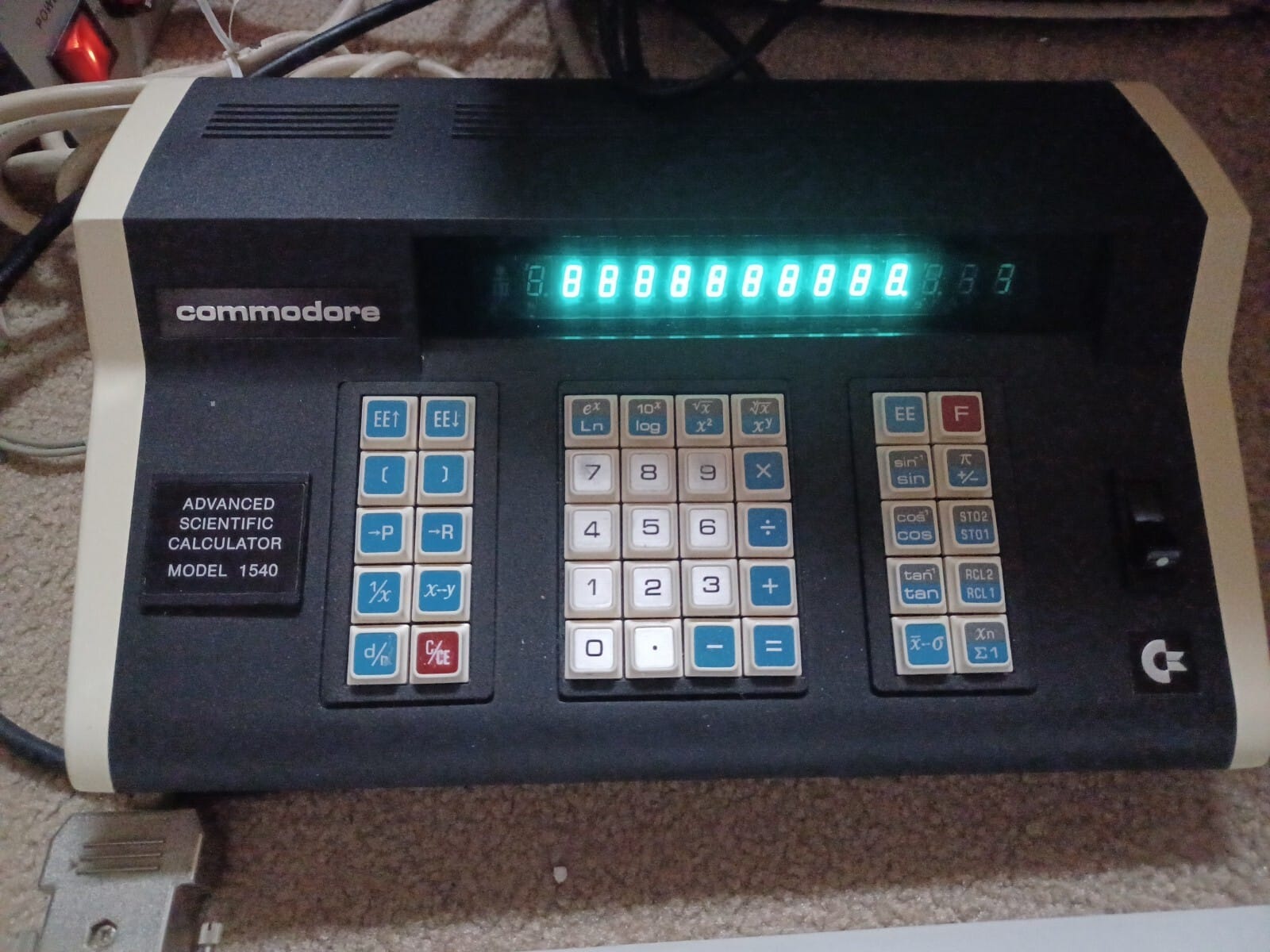 A Commodore branded "Advanced Scientific Calculator Model 1540". 10-digit, blue digital readout. In addition to the normal keypad and operators, we have log, exponents, cos, sin, tan, and other buttons I cannot decipher.