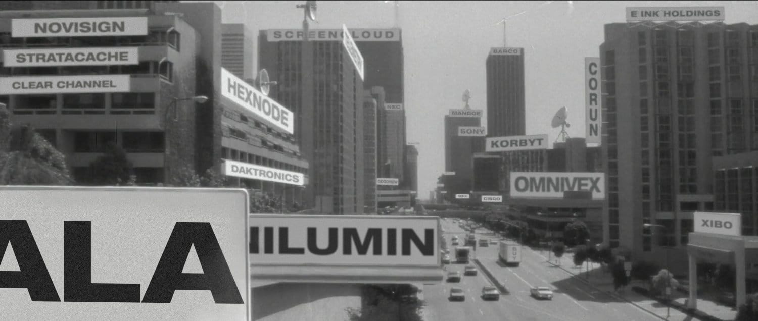 Still image from the movie They Live, in which all signage across the city shows its subliminal message. I have replaced all original text like "Reproduce" and "Obey" with the names of many digital signage companies that control the industry. Novisign, Stratacache, Clear Channel, Omnivex, Hexnode, and more.