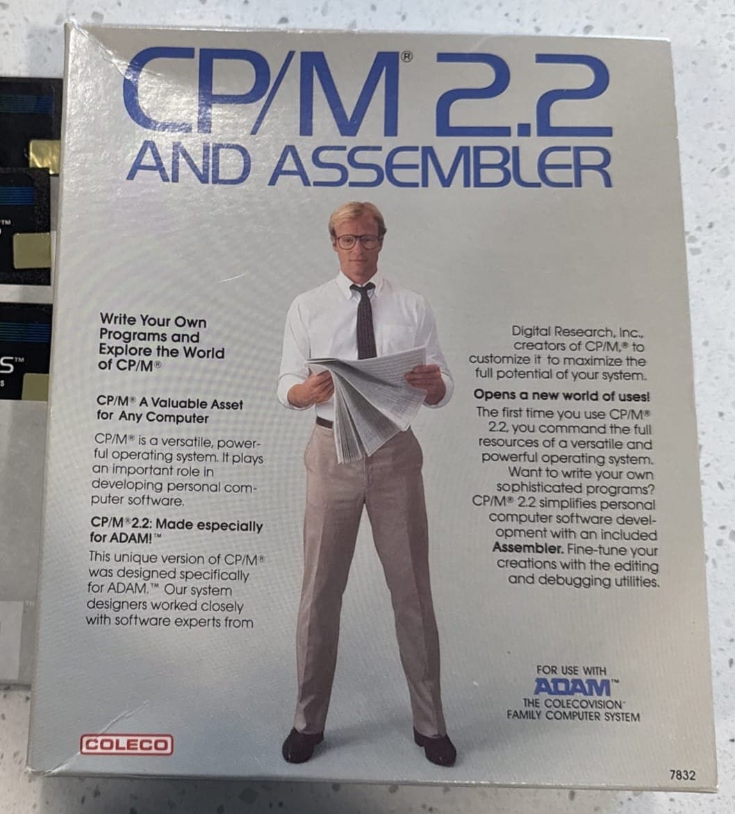 Retail box for “CP/M 2.2 and Assembler” for the Coleco ADAM computer. The white packaging features large blue “CP/M 2.2” lettering and promotional text describing the operating system and included assembler. A man in business attire stands centered on the cover reading a newspaper.