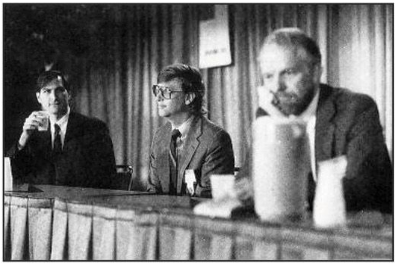 Fairly famous shot of Steve Jobs looking on with interest at John Warnock who looks glum as hell. Bill Gates sits in the middle looking like a smug nerd. Warnock has his back turned to Gates.